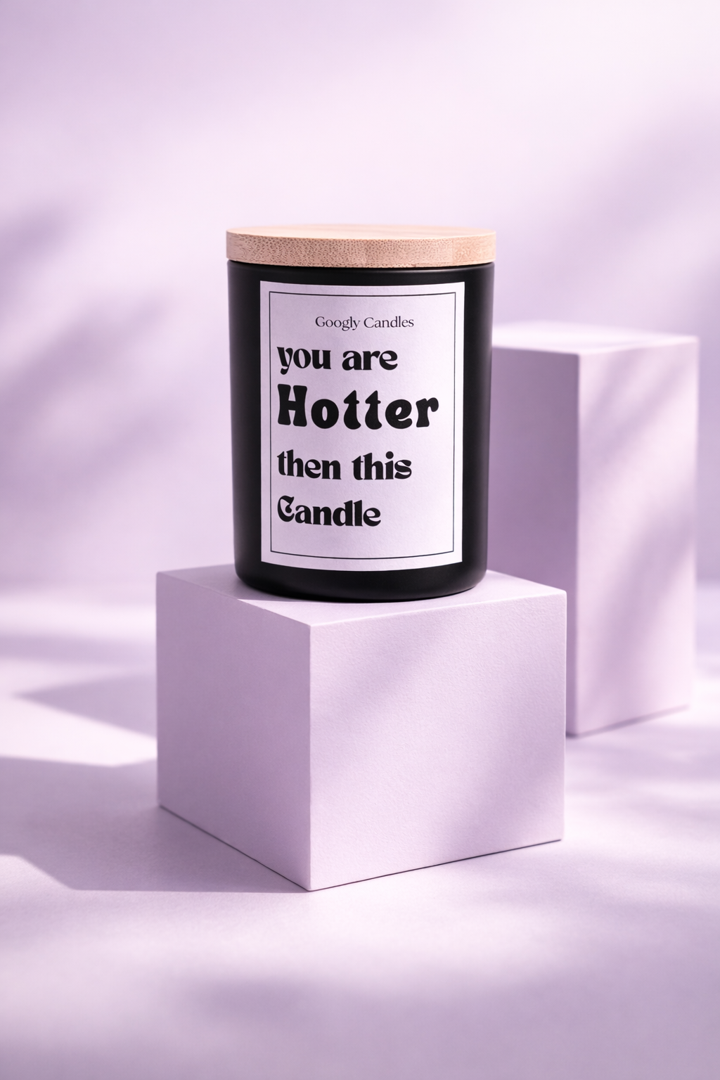 Candle with a humorous label on a white cube against a light purple background