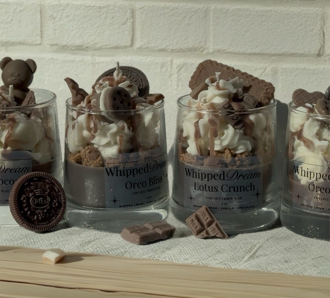 Four glass jars with candles desserts whipped cream, cookies, and chocolate pieces on a white brick wall background.